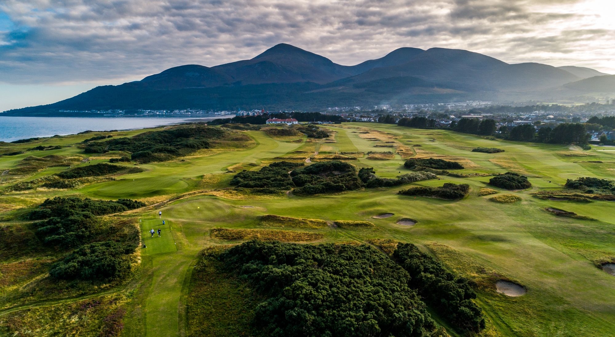 A scenic view of the Royal County Down golf course, showcasing its lush green fairways and the surrounding natural landscape.