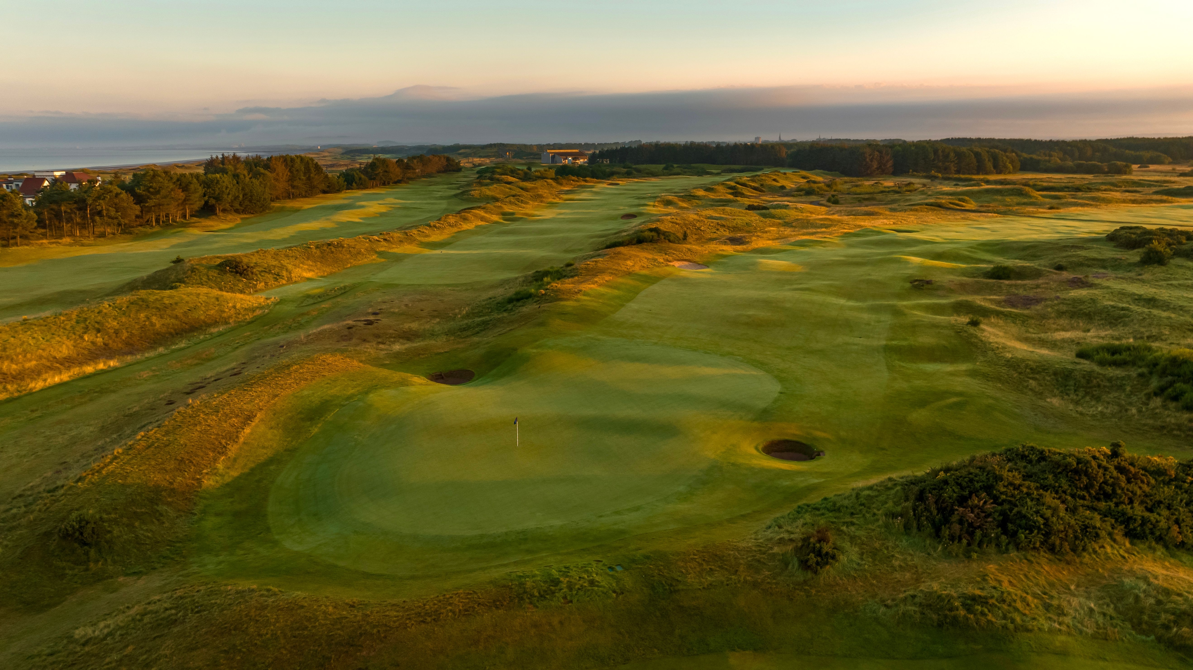 View of Dundonald Links golf course with rolling green fairways, bunkers, and distant trees under a bright, slightly cloudy sky