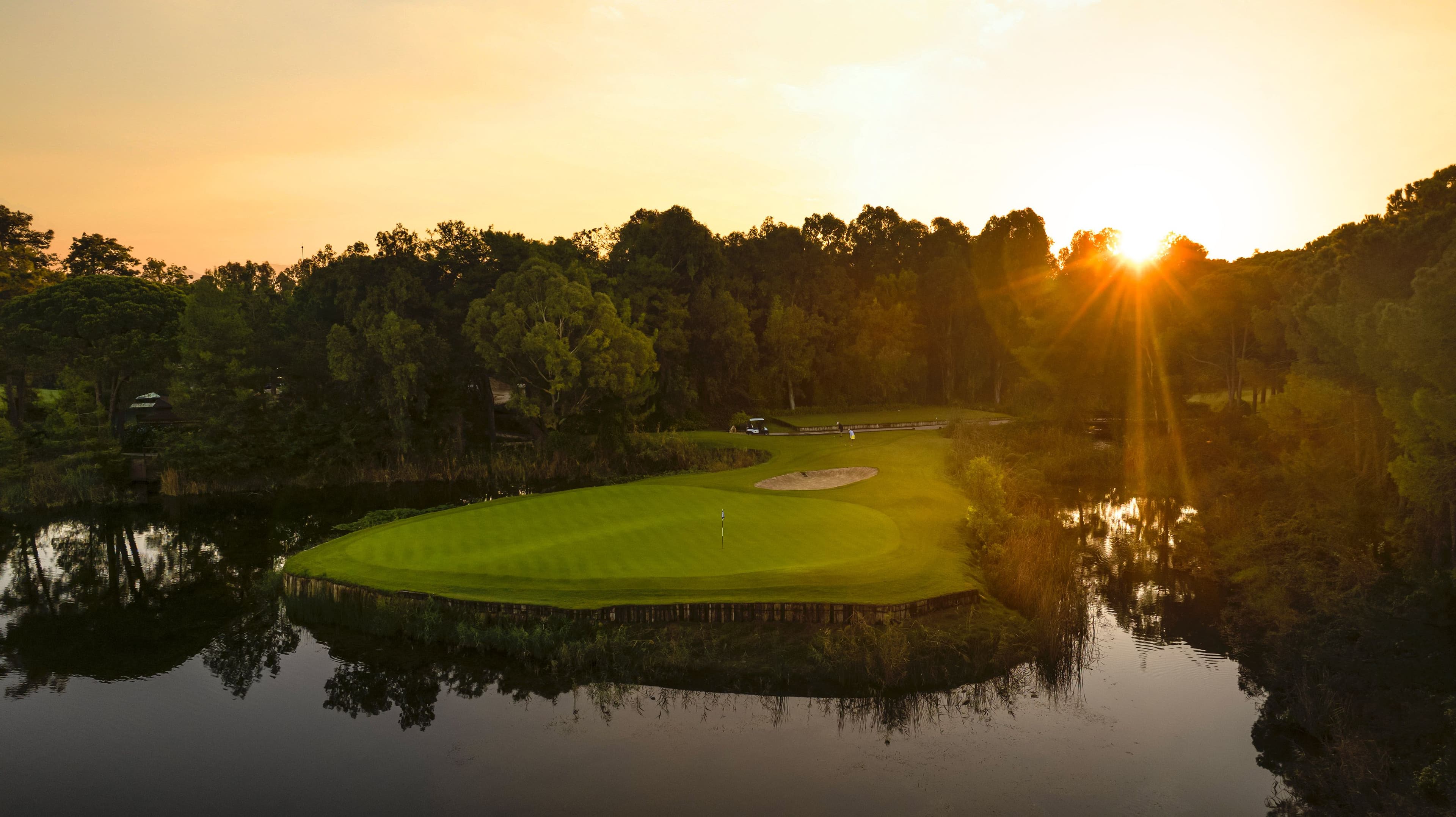 A wide view of the National Golf Course with manicured fairways, bright green grass, and surrounding trees under a clear sky.