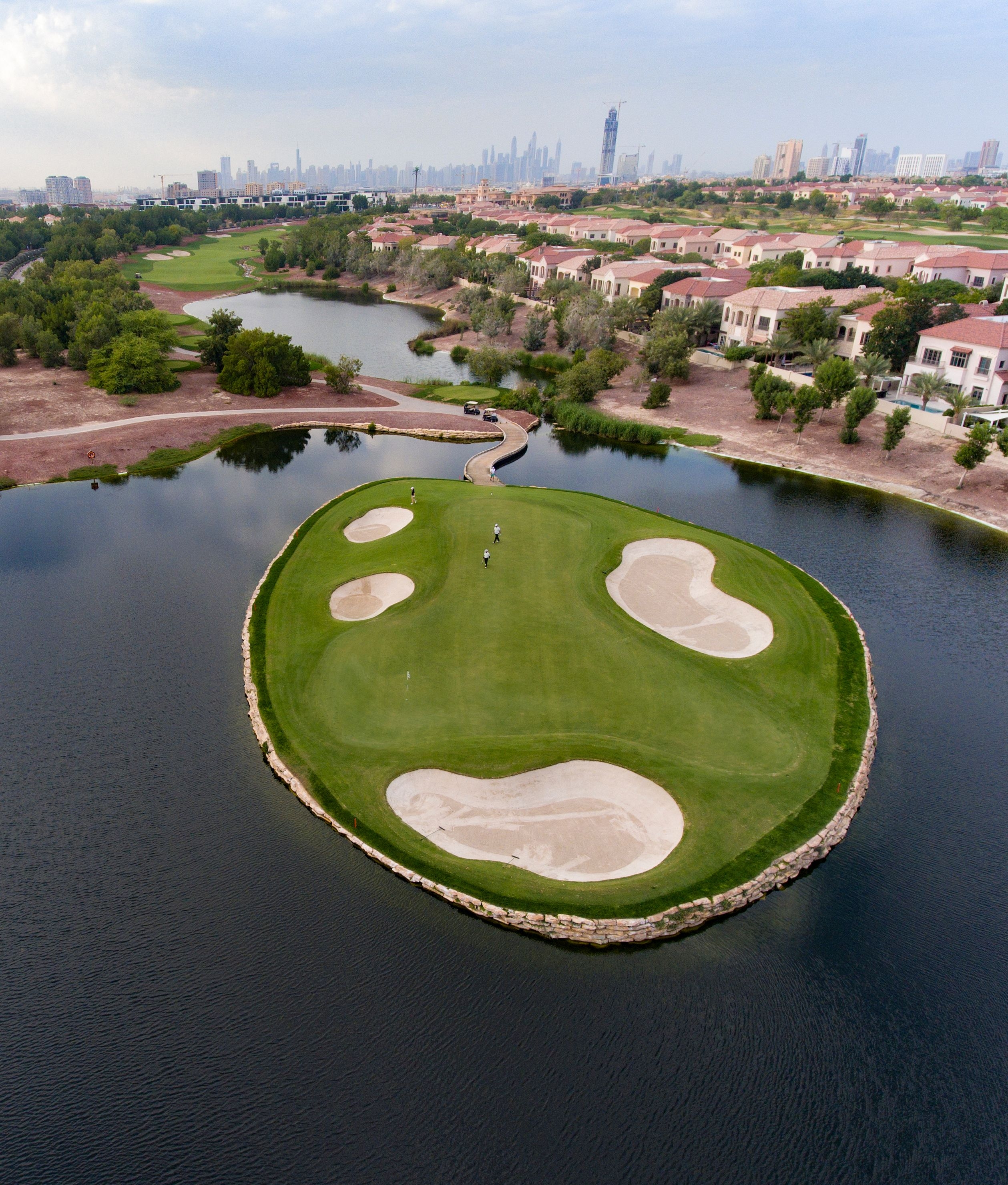 Aerial view of the lush green Earth Course golf course in Dubai, with manicured fairways, sand bunkers, and the city skyline in the distance