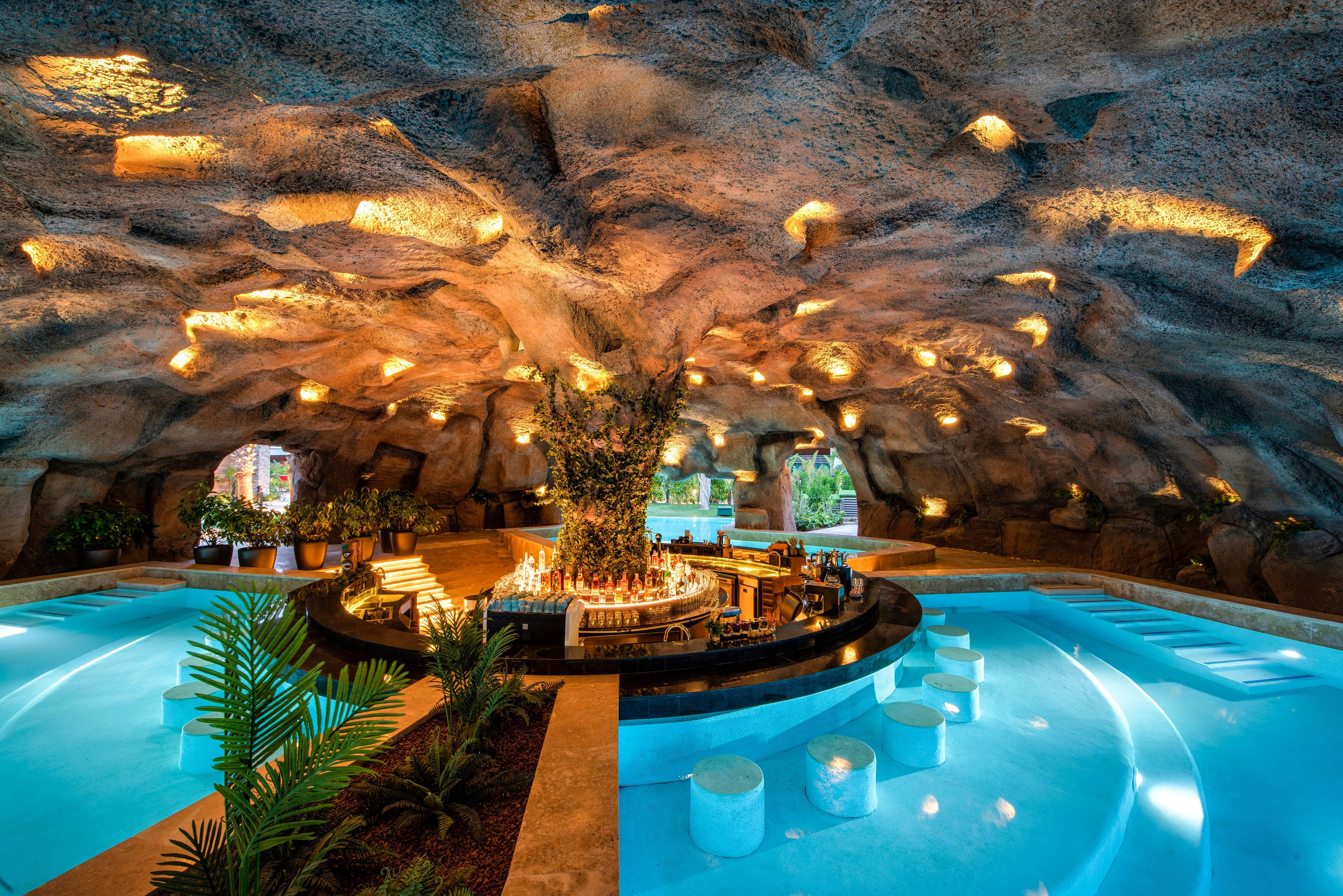 Indoor cave-like spa pool at Regnum resort, with turquoise water, rock walls, soft lighting, and guests relaxing in the crown pool area