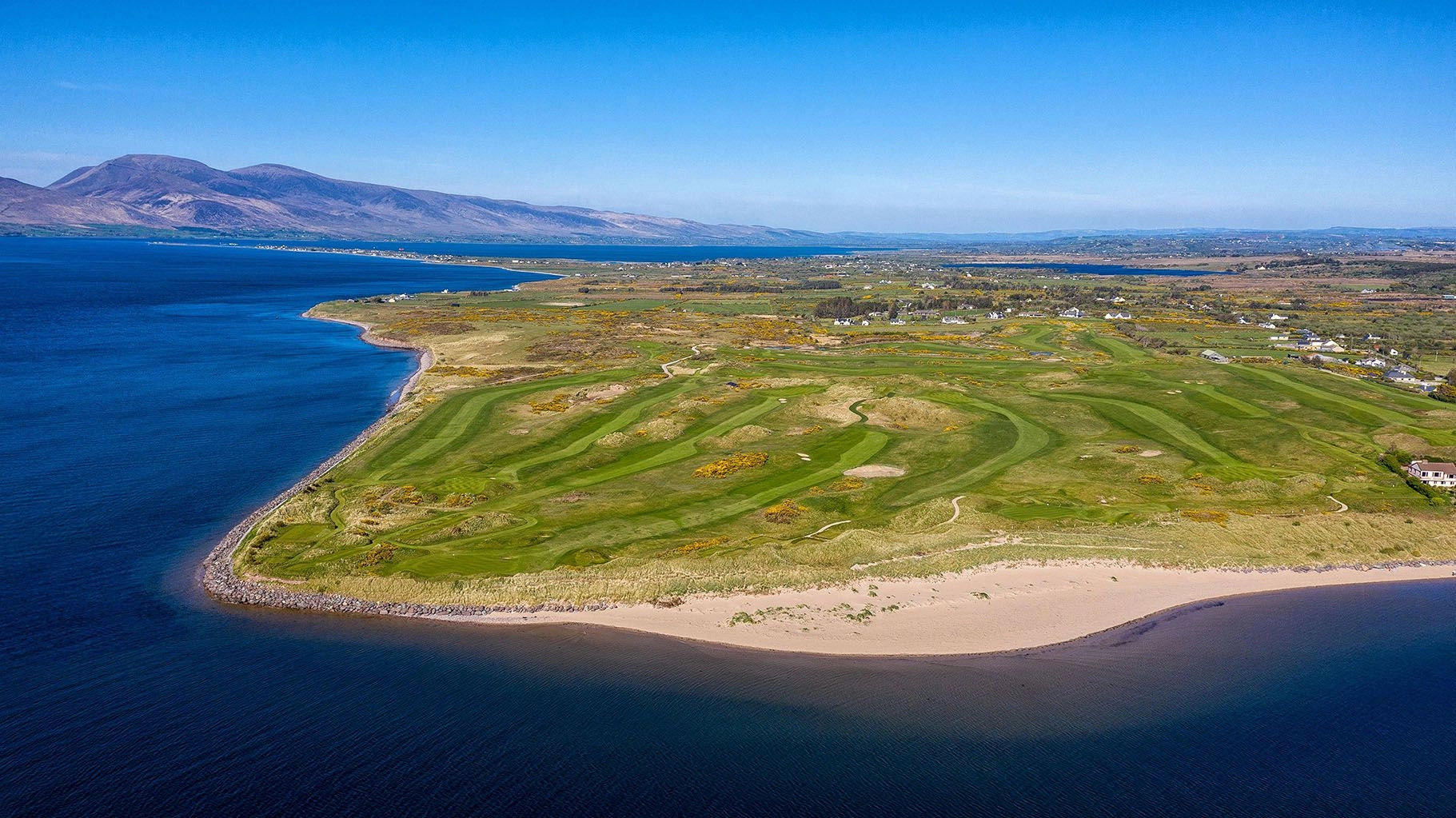 View over Dooks Golf Club with rolling green fairways, bunkers, and distant hills under a bright sky on the Irish coastline