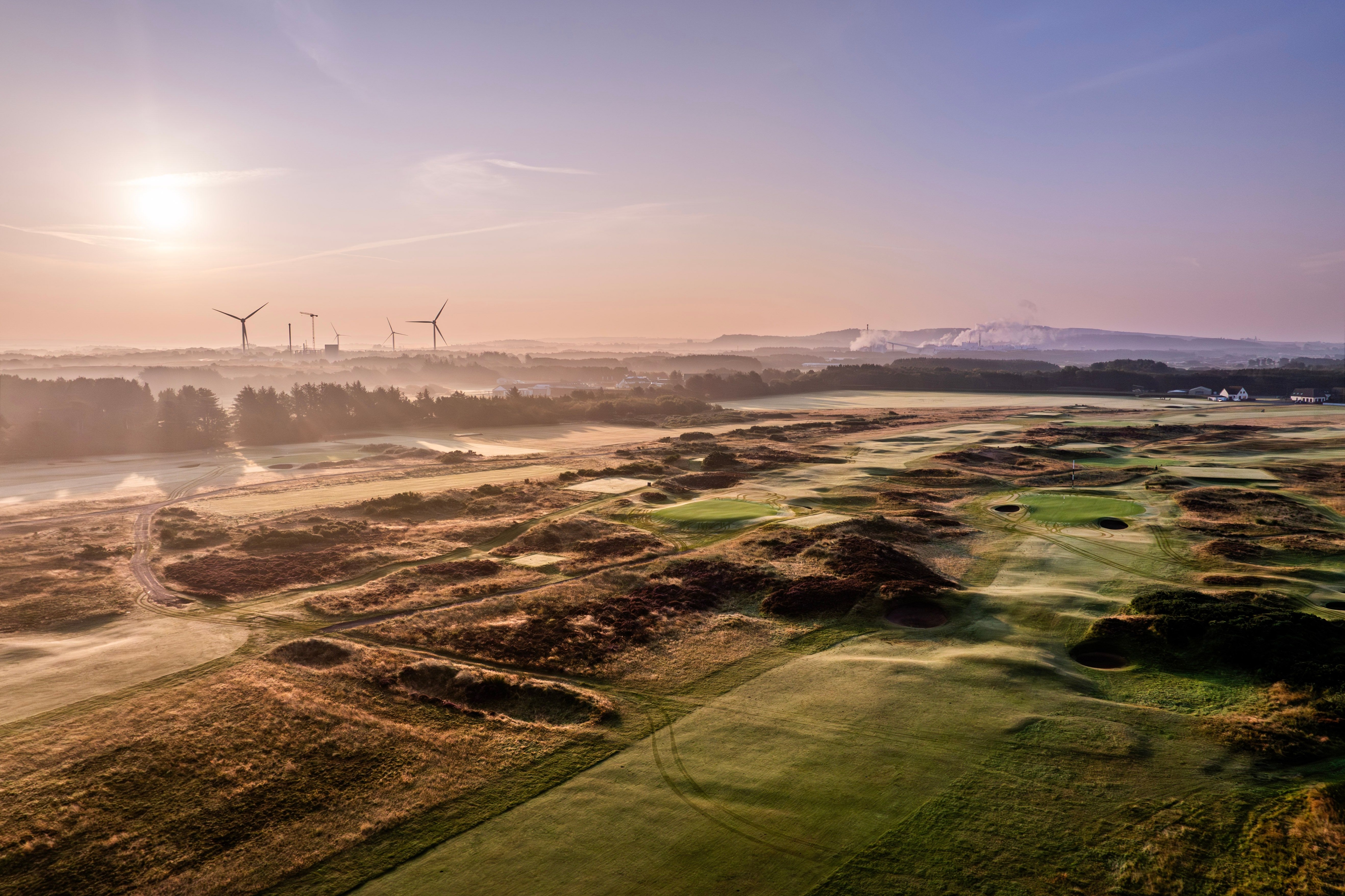 View across the Glasgow Gailes links golf course with rolling dunes, pot bunkers, and distant clubhouse under a cloudy Scottish sky